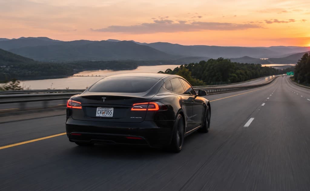 Luxury sedan driving along a lakeside highway at sunset
